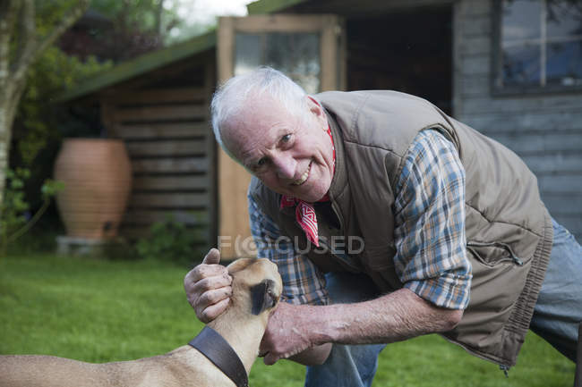 Hombre mayor, acariciando perro mascota en el jardín - foto de stock