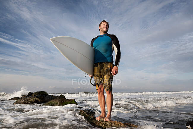 Surfista em pé sobre rochas na praia — Fotografia de Stock