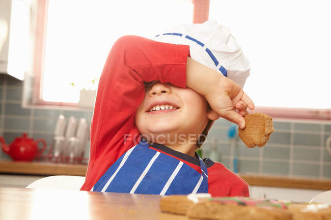 Young boy eating cookie in kitchen — Stock Photo
