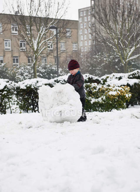 Хлопчик будує сніговика в парку — стокове фото