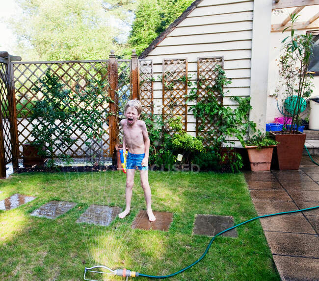 Мальчик играет в разбрызгиватель на заднем дворе — стоковое фото