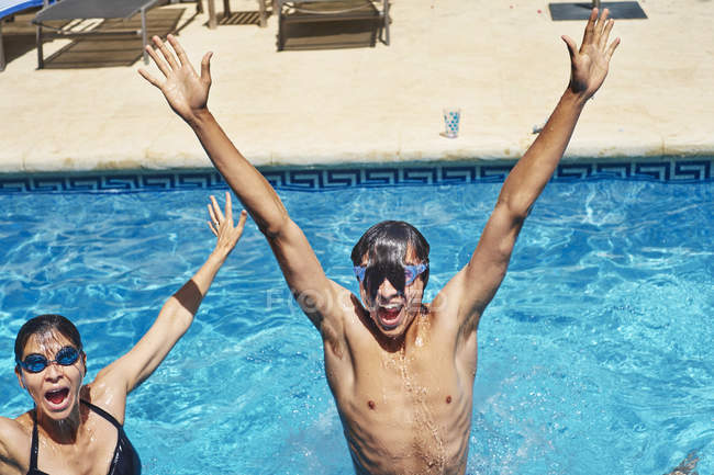 Portrait of young man and mother with hands raised in swimming pool — Stock Photo