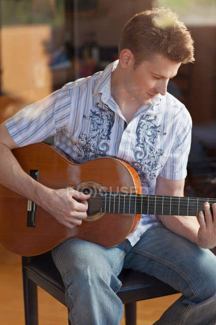 Homme jouant de la guitare dans le salon — Photo de stock