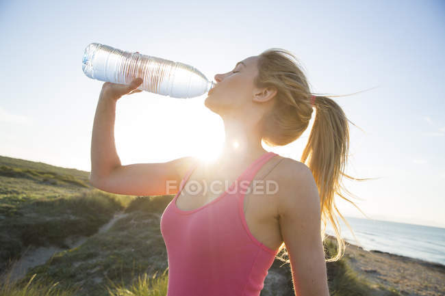 Junge Frau am Strand, trinkt aus Wasserflasche — Stockfoto