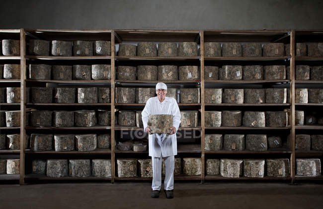Man holding large cheese in warehouse — Stock Photo