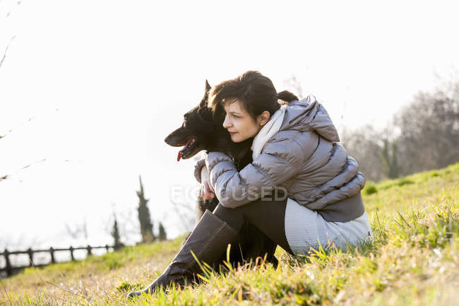 Mulher adulta média e seu cão sentado na encosta — Fotografia de Stock