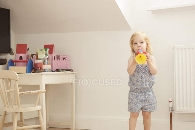 Портрет малюка-жінки в ігровій кімнаті, що грає іграшкову трубу — стокове фото