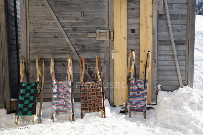 Row of four sledges leaning against log cabin — Stock Photo