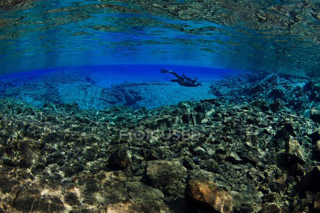 Buceador nadando por formaciones rocosas - foto de stock