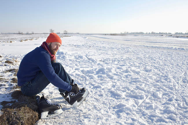 Man lacing up ice skates in snowy field — Stock Photo