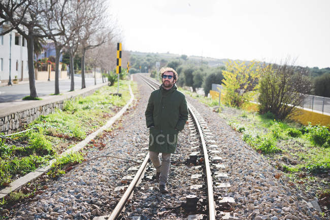 Homme adulte moyen portant des lunettes de soleil se promenant sur la voie ferrée — Photo de stock