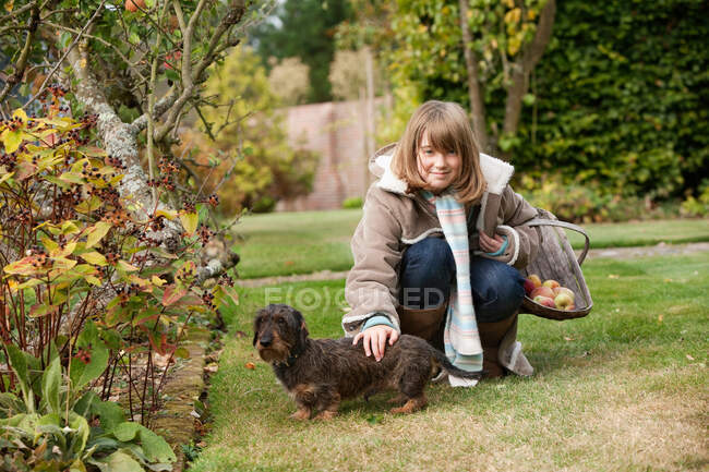 Chica con cesta y perro en el jardín - foto de stock