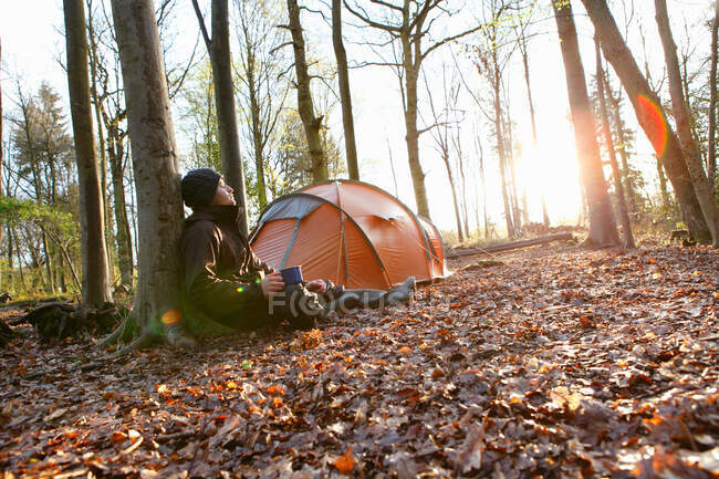 Man drinking coffee by tent in forest — Stock Photo