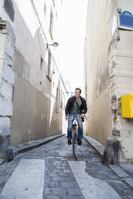 Средний взрослый мужчина на велосипеде по узкой булыжной улице, Париж, Франция — стоковое фото
