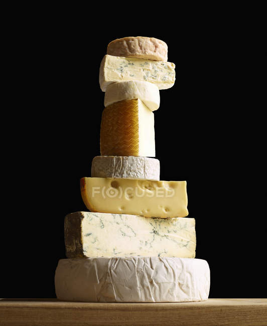 Stack of selection of cheeses, against black background — Stock Photo