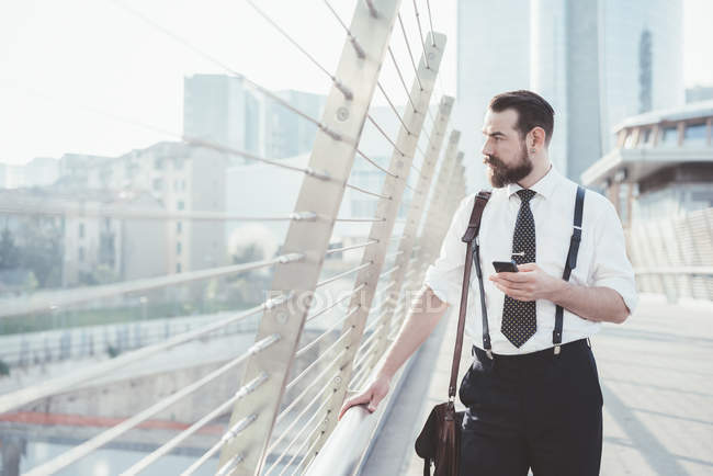 Elegante uomo d'affari con smartphone che guarda fuori dalla passerella della città — Foto stock