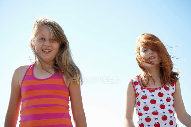 Smiling girls hair blowing in wind against sky — Stock Photo