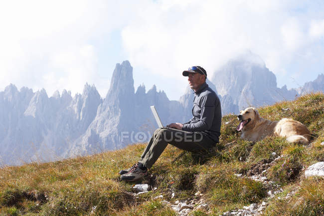 El hombre y el perro en las montañas con portátil - foto de stock