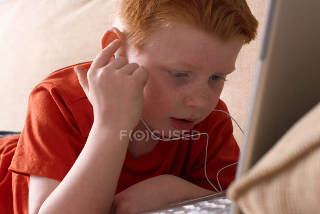 Boy in headphones using laptop on couch — Stock Photo