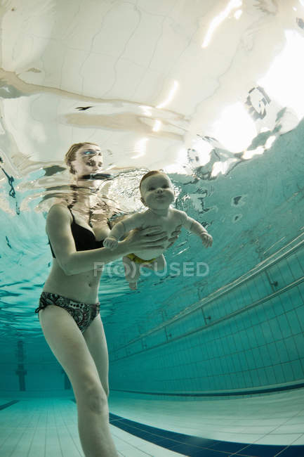 Mulher ensinando bebê a nadar na piscina — Fotografia de Stock
