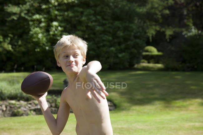 Хлопчик в саду кидає м'яч регбі — стокове фото