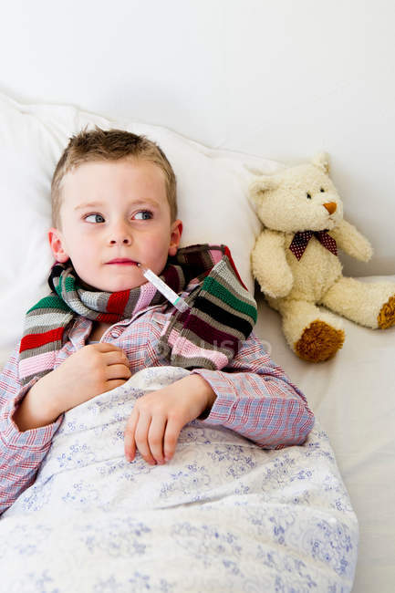 Niño con termómetro en la boca en la cama - foto de stock