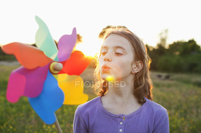 Menina soprando moinho de vento brinquedo ao pôr do sol — Fotografia de Stock