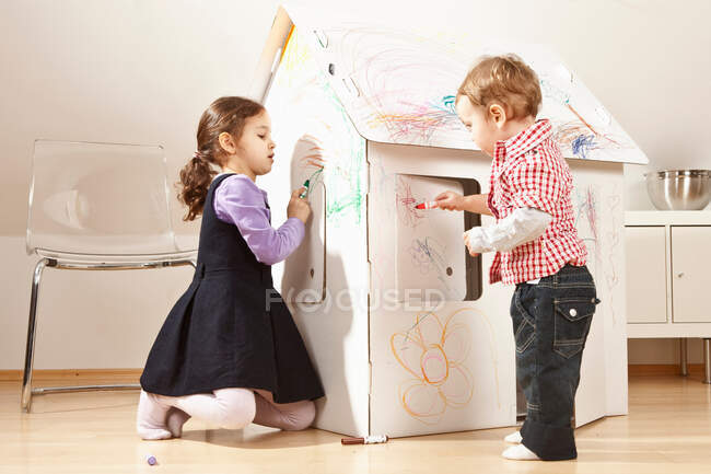 Мальчик и девочка рисуют картонный домик — стоковое фото