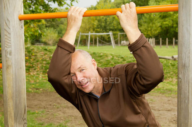 Older man hanging from jungle gym — Stock Photo