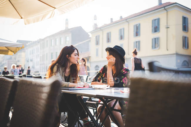 Дві молоді жінки спілкуються у тротуарному кафе — стокове фото