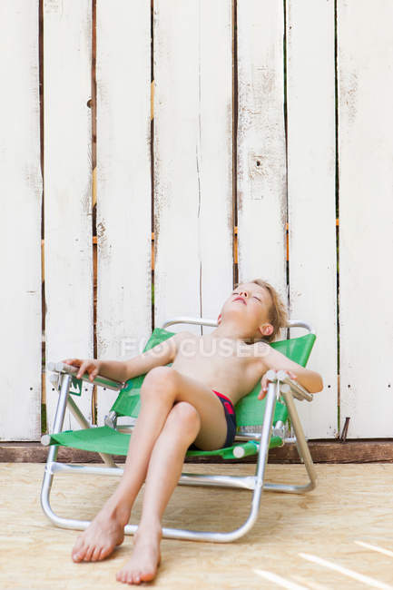 Niño en traje de baño en silla de jardín en interiores - foto de stock