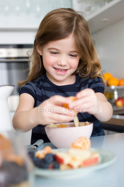 Girls putting fruit into her yogurt — Stock Photo