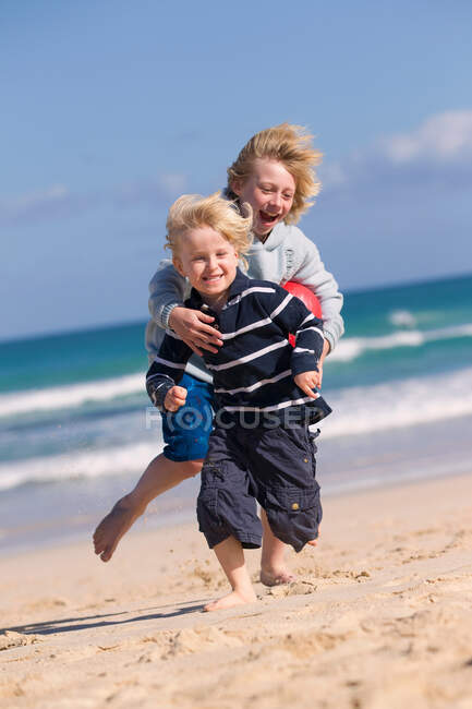 Garçons jouant avec boule rouge sur la plage — Photo de stock