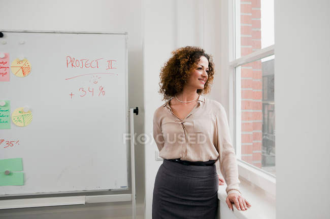 Femme d'affaires souriant à la fenêtre du bureau — Photo de stock