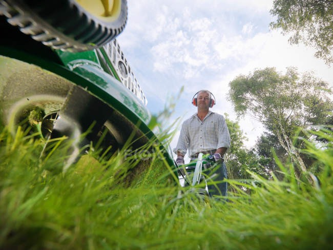 Садовник с защитными ушами для стрижки газона с газонокосилкой, вид на поверхность — стоковое фото