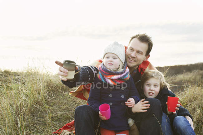 Smiling mid adult man with daughter and son on sand dunes — Stock Photo