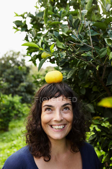 Woman balancing mandarin on her head — Stock Photo