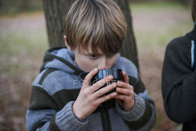 Boy drinking hot drink in autumnal forest — Stock Photo
