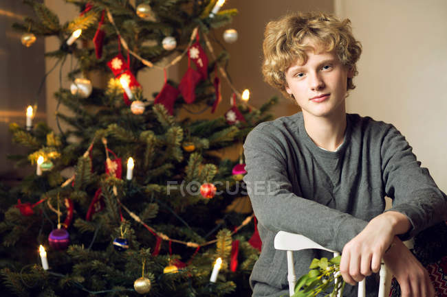 Adolescente sentado na árvore de Natal — Fotografia de Stock