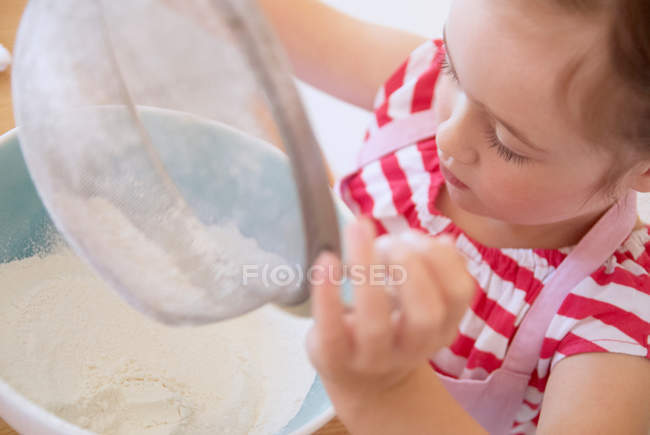 Girl sifting flour in kitchen — Stock Photo