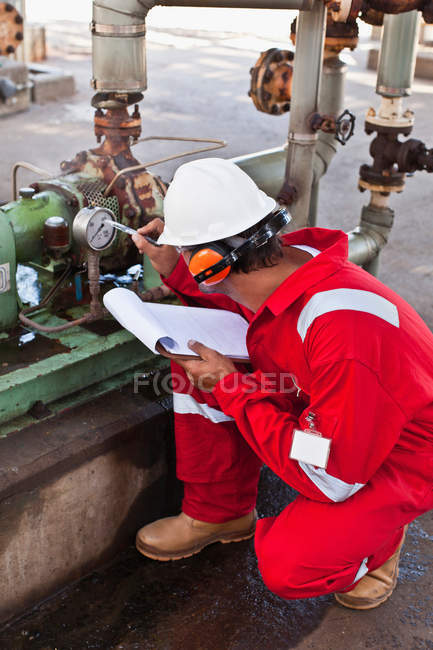 Worker noting gauge at oil refinery — Stock Photo