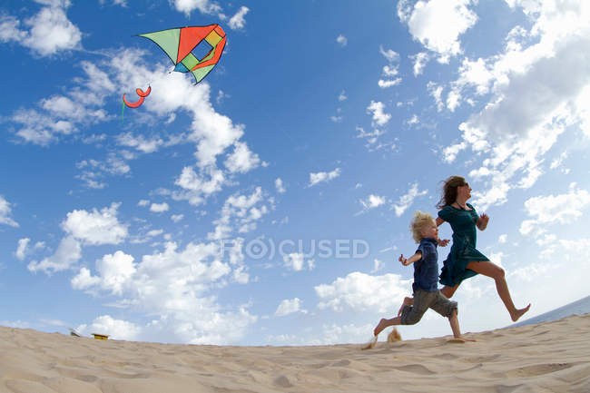 Madre e hijo volando cometa en la playa - foto de stock
