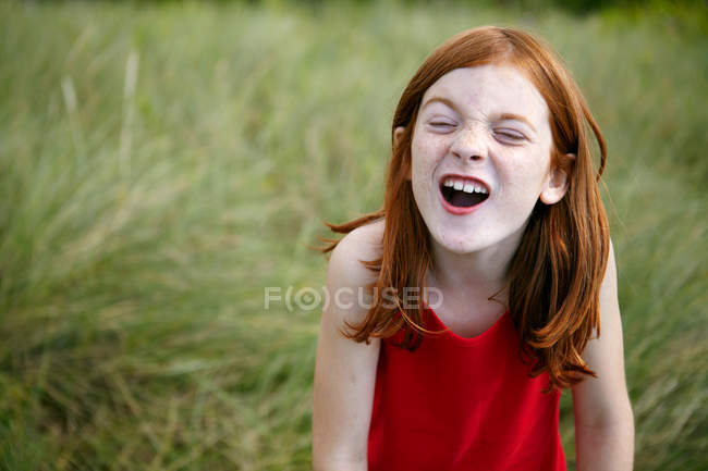Дівчина посміхається у високій траві, фокус на передньому плані — стокове фото