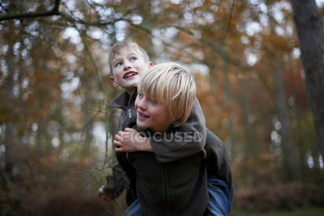 Menino dando amigo piggyback através de floresta outonal — Fotografia de Stock