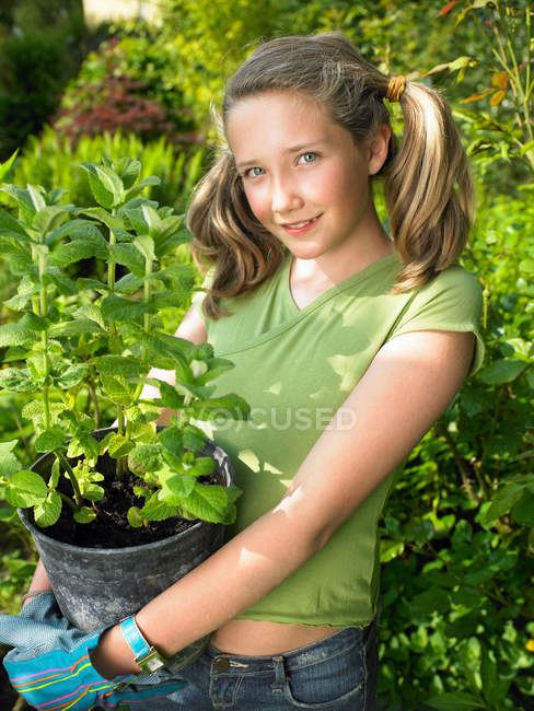 Улыбающаяся девушка держит растение в горшке — стоковое фото