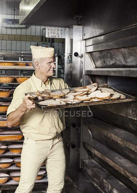 Счастливый пекарь кладет в духовку кусочек нарезанного хлеба — стоковое фото