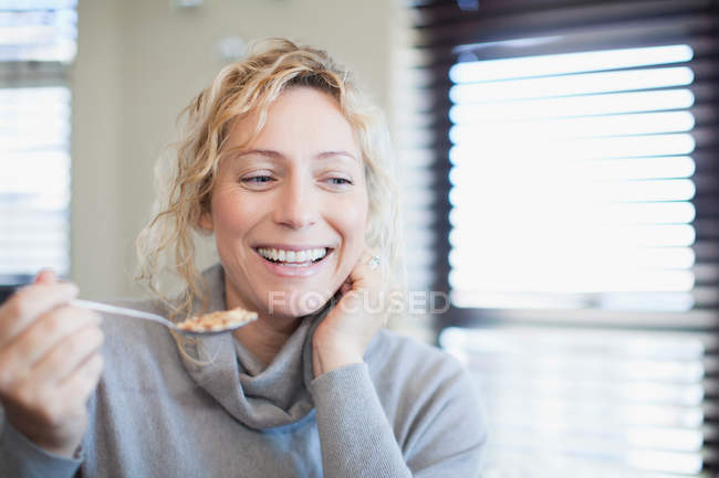 Усміхнена жінка їсть зернові в приміщенні — стокове фото