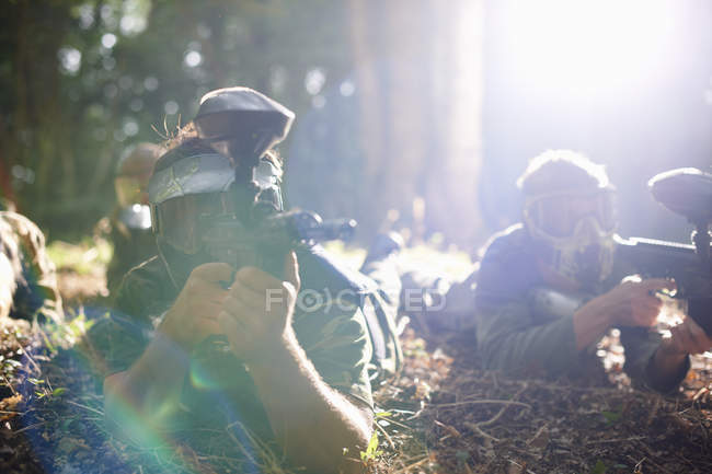 Пейнтболісти лежать на землі в лісі під сонячним світлом в дії — стокове фото