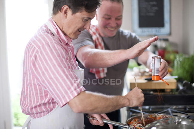 Mature men cooking, one stirring and one adding spices — Stock Photo
