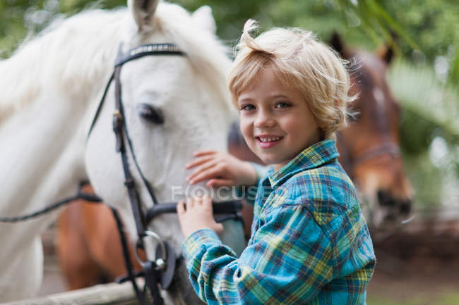 Smiling boy petting horse in yard, focus on foreground — Stock Photo